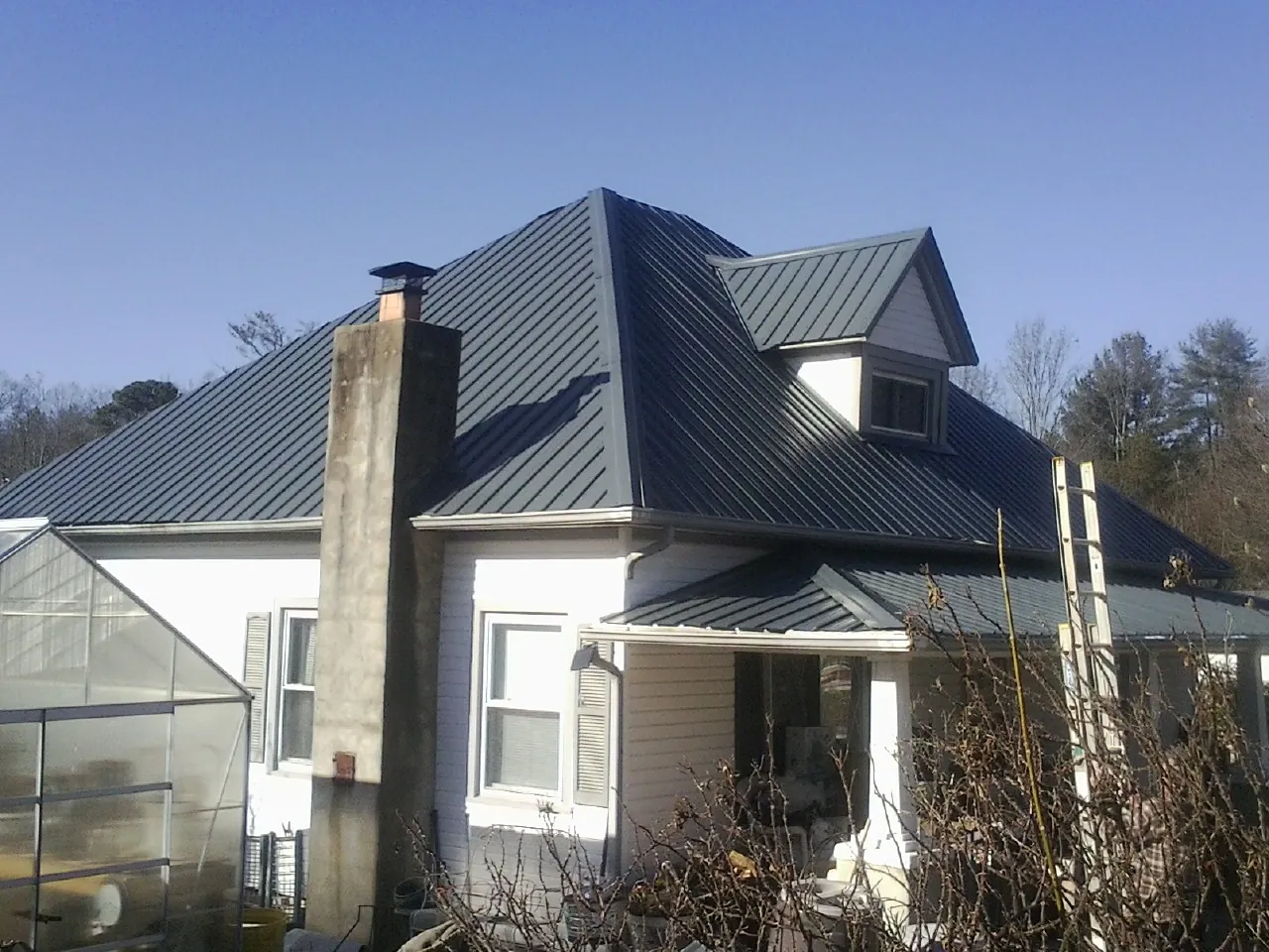 Dark blue standing seam metal roof on a white farmhouse with dormer — Slate & Tile Roof Repair by Roofing Brothers in Durand
