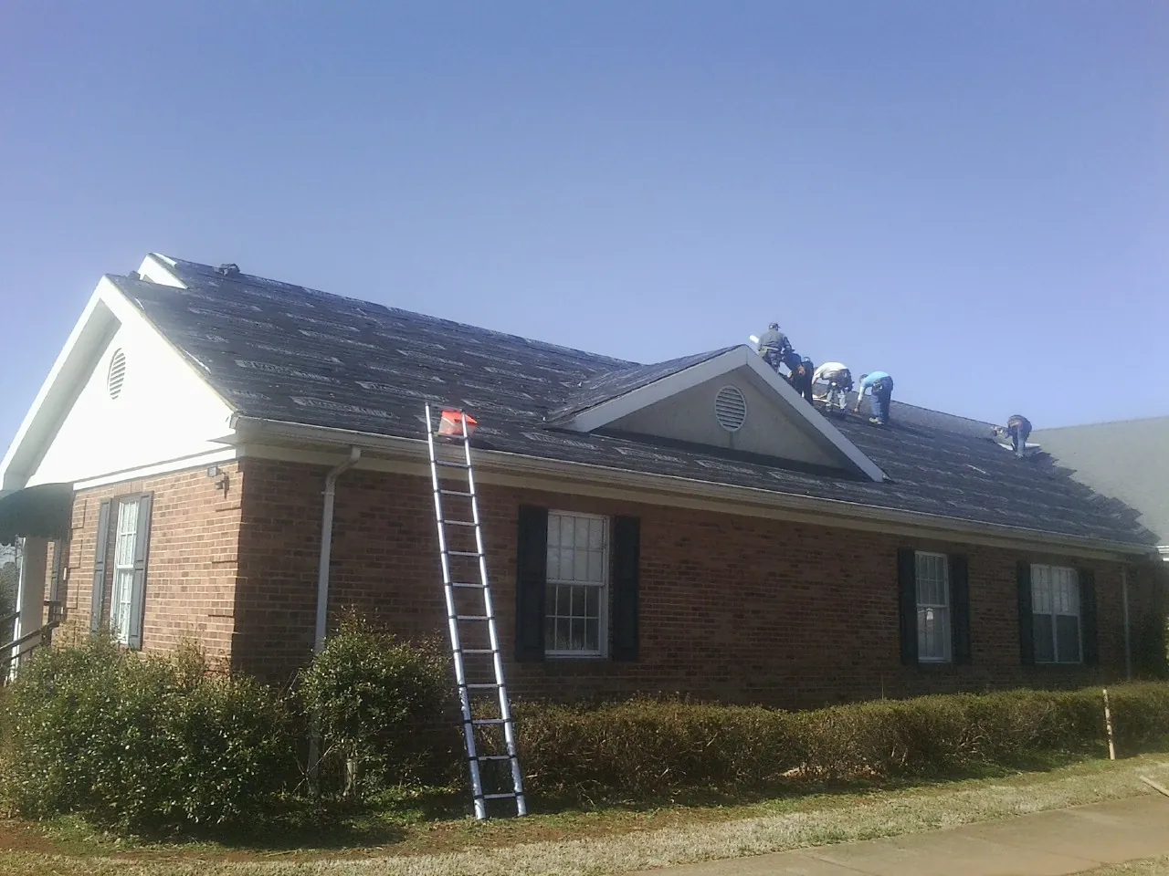 Crew tearing shingles off a brick ranch roof with a ladder set — Emergency Roof Repair work by our crew in Durand