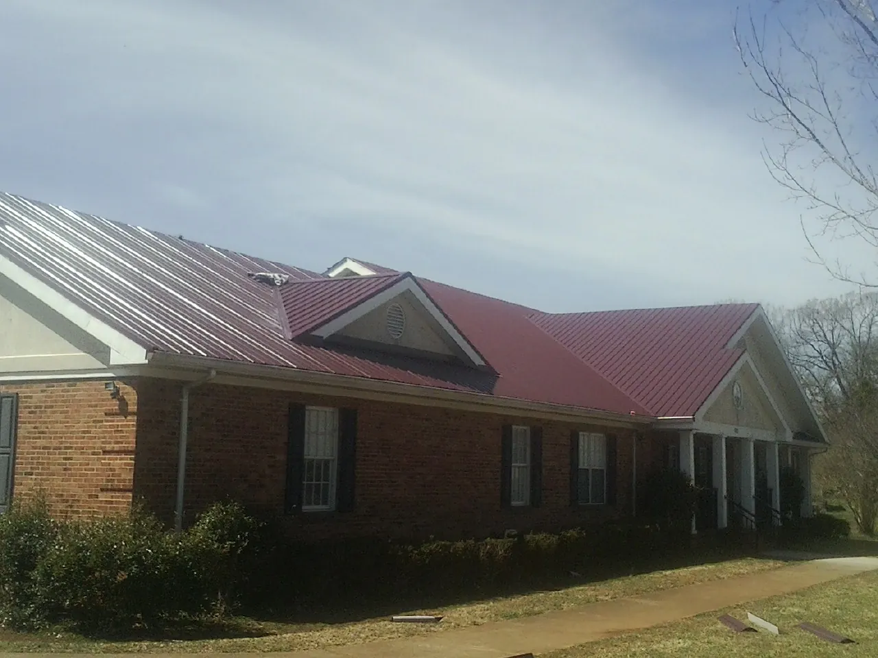 Red metal roof with gabled entries on a long brick building, from a Hail Damage Roof Repair job in Durand
