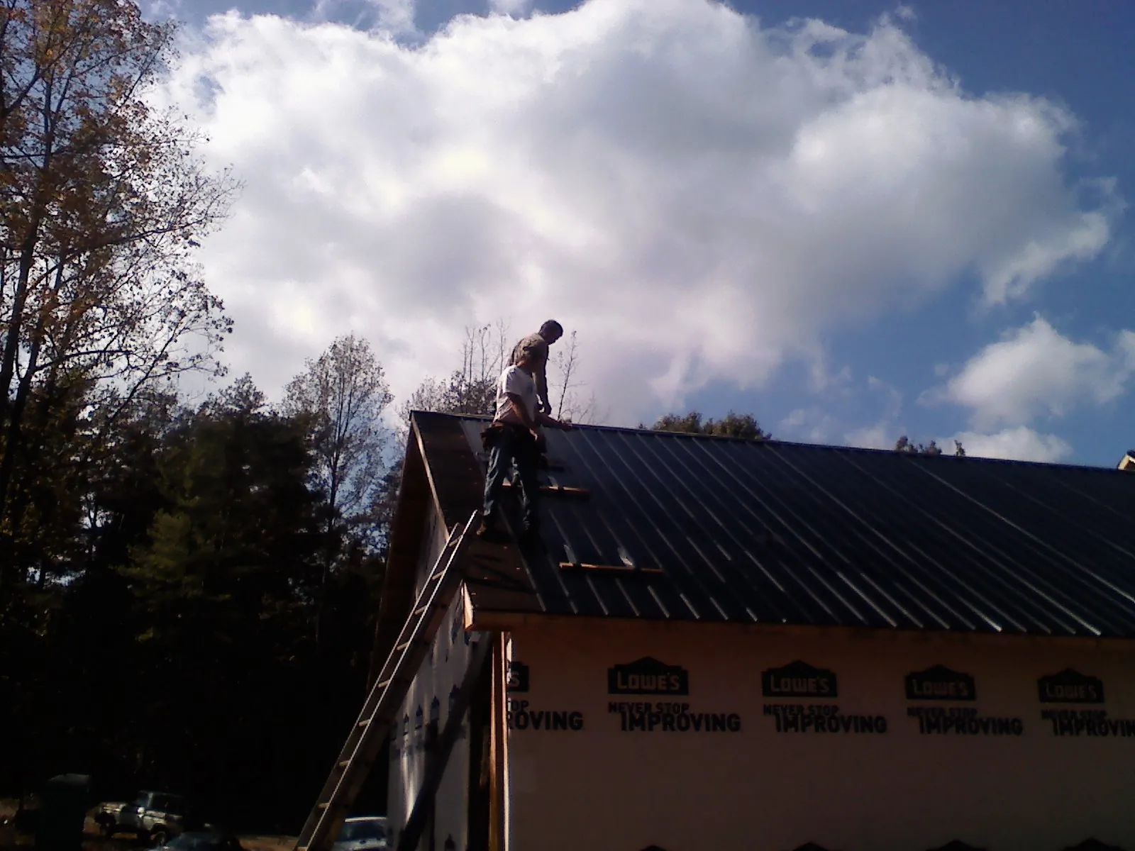 Roofer fastening dark metal panels high against a cloudy sky, from a Roof Inspection job in Durand
