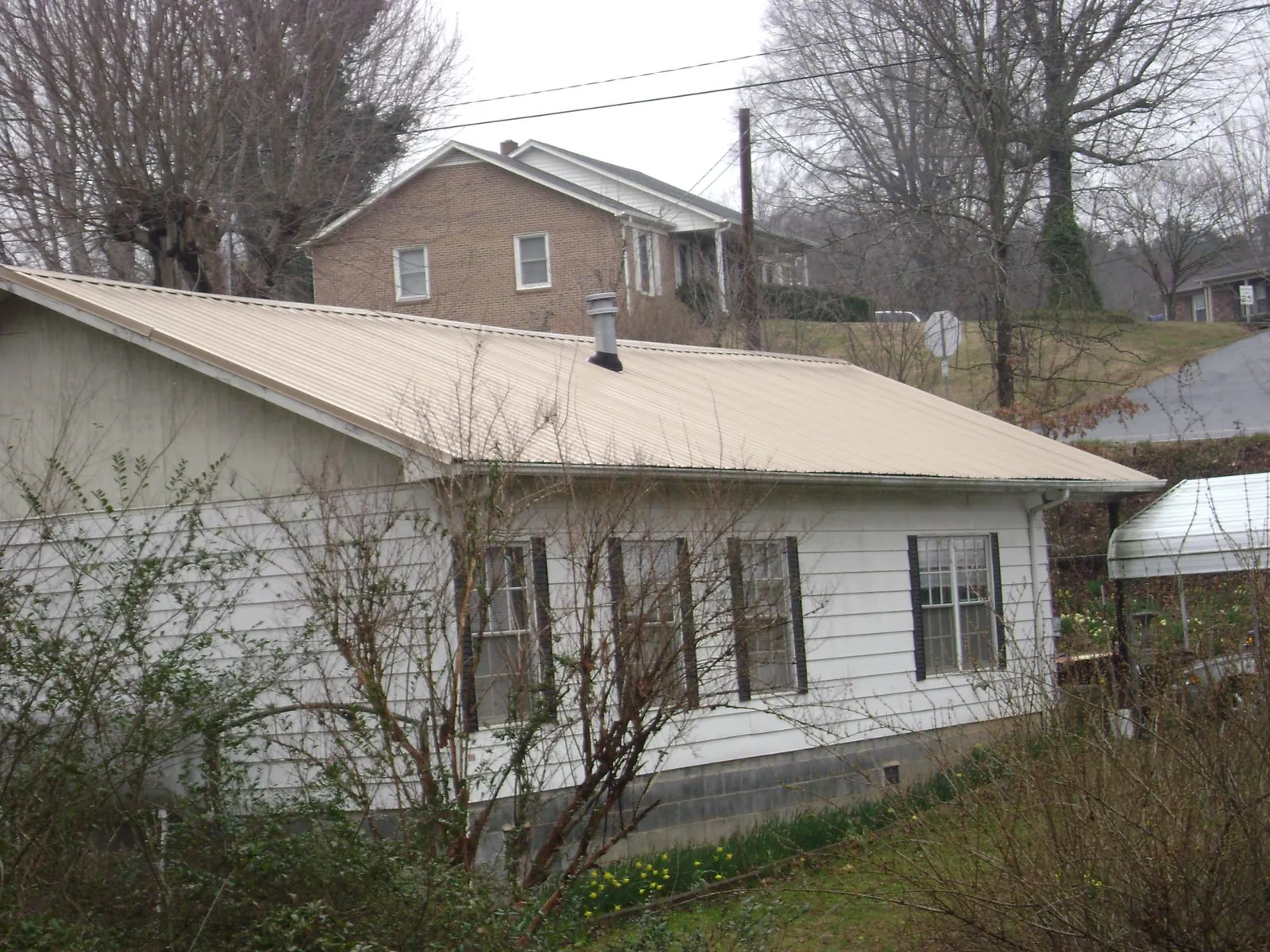 Tan metal roof on a white sided house set into a hillside — Commercial Roofing by Roofing Brothers in Durand
