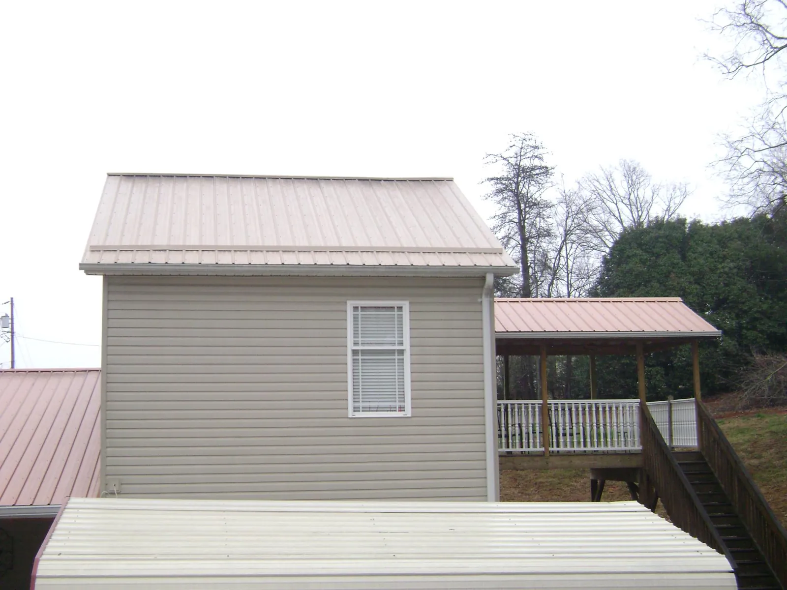 Tan metal roofs on a two story addition and attached porch, from a Roof Replacement job in Durand