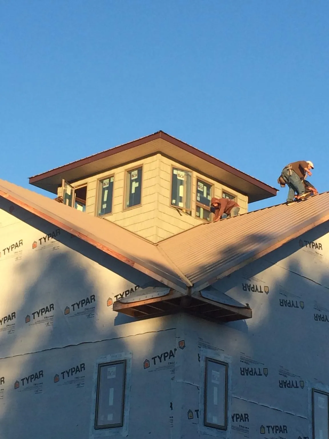 Roofers working around a rooftop cupola on a new metal roof at sunset — Roof Waterproofing in Durand by Roofing Brothers